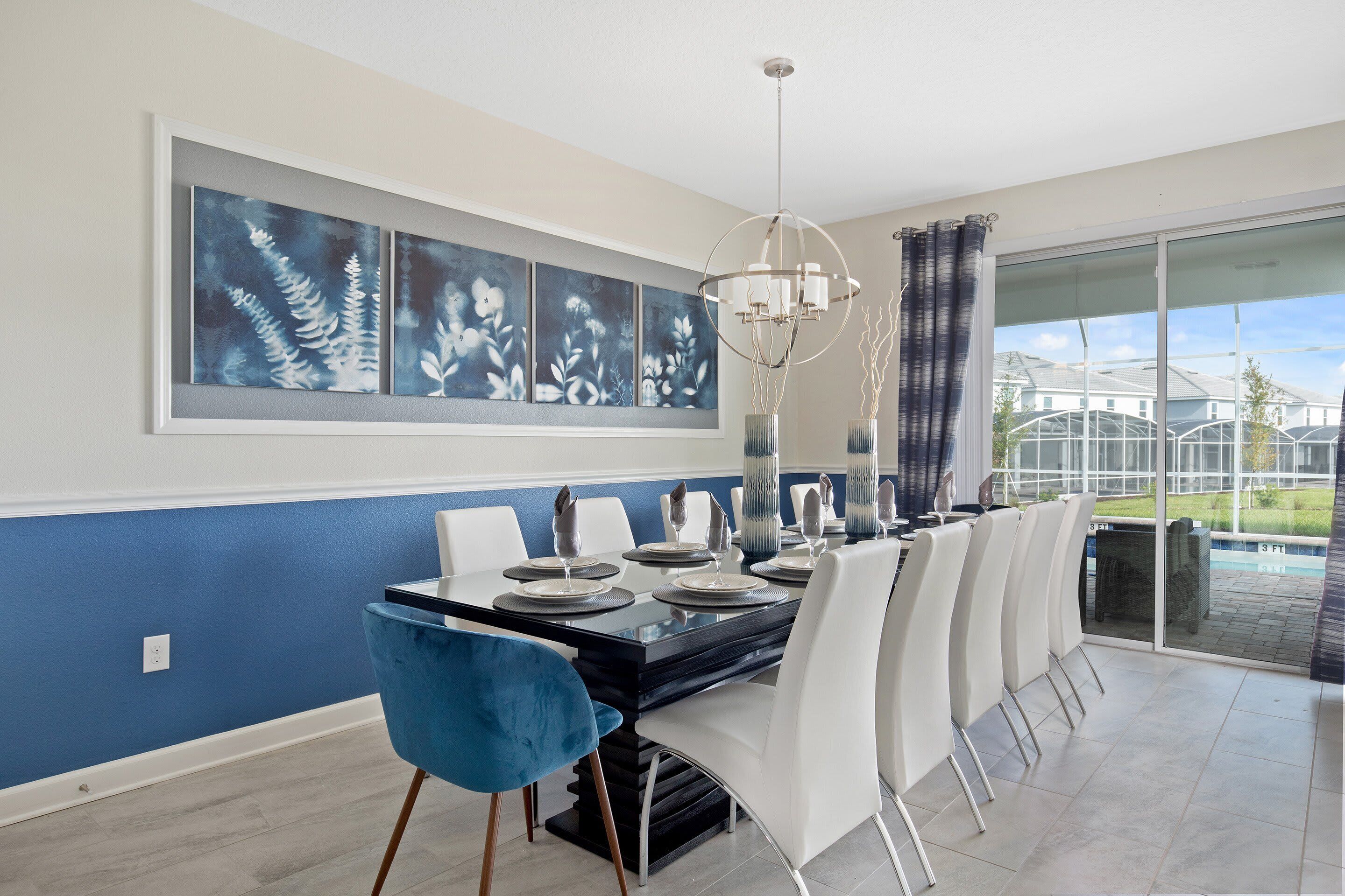 Un coin repas avec une table noire, des chaises blanches et un lustre. Trois œuvres d’art encadrées sont accrochées au mur au-dessus de la table.