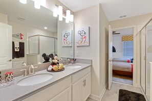 A bathroom with two sinks, a large mirror, and Mickey Mouse decorations.