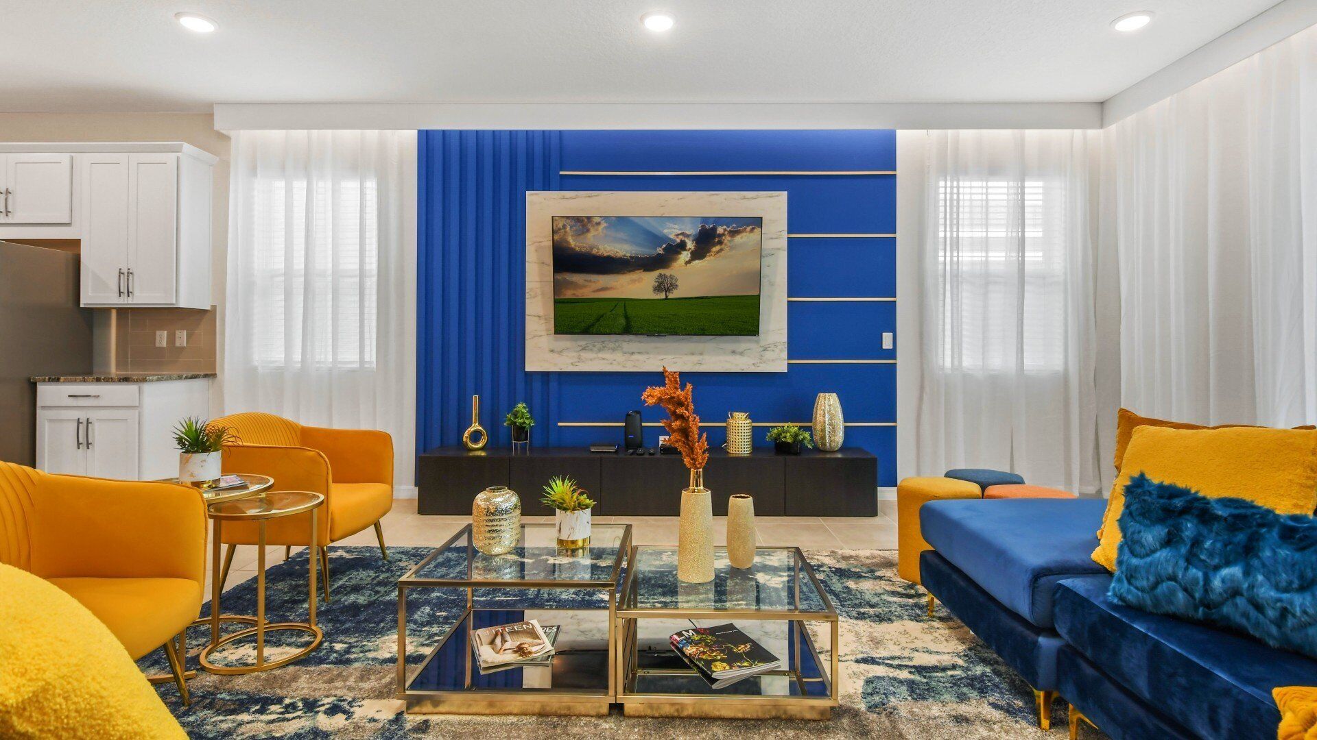 A modern living room with a blue accent wall, a large flat-screen TV, and a mix of yellow and blue furniture.