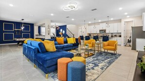 Una sala de estar moderna con un sofá azul, cojines amarillos y anaranjados, una mesa de centro y una escalera que sube al piso superior.