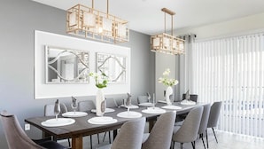 Une salle à manger moderne avec une longue table, des chaises grises et des luminaires suspendus.