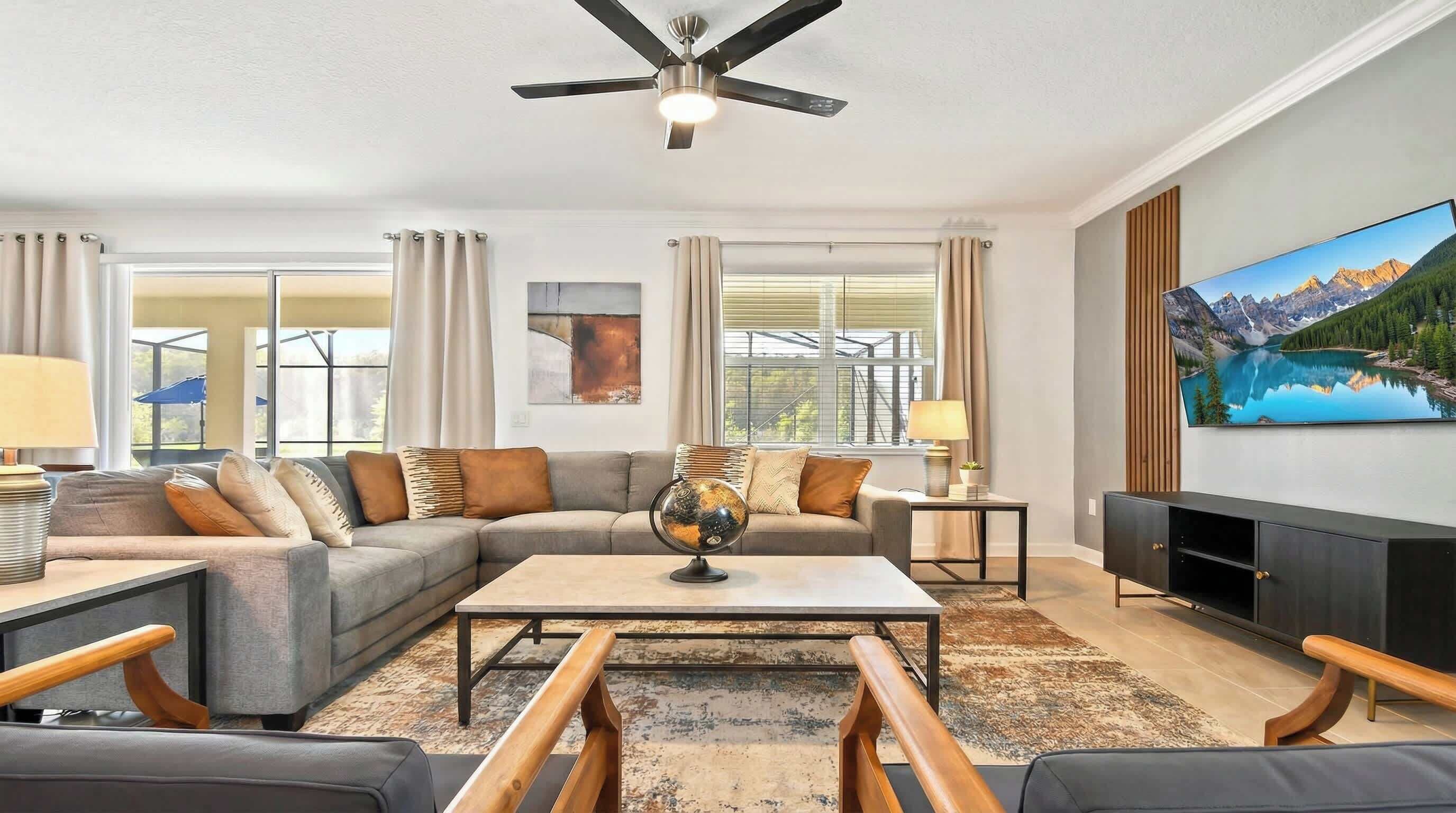A modern living room with a sectional sofa, a coffee table, a globe, and a large TV.