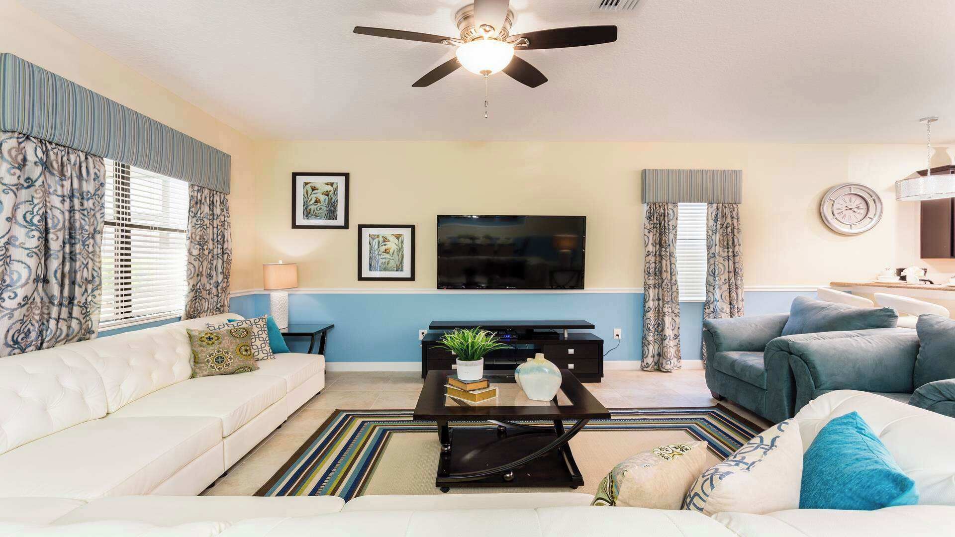 A living room with a sofa, a coffee table with decorative items, a TV, and a ceiling fan.