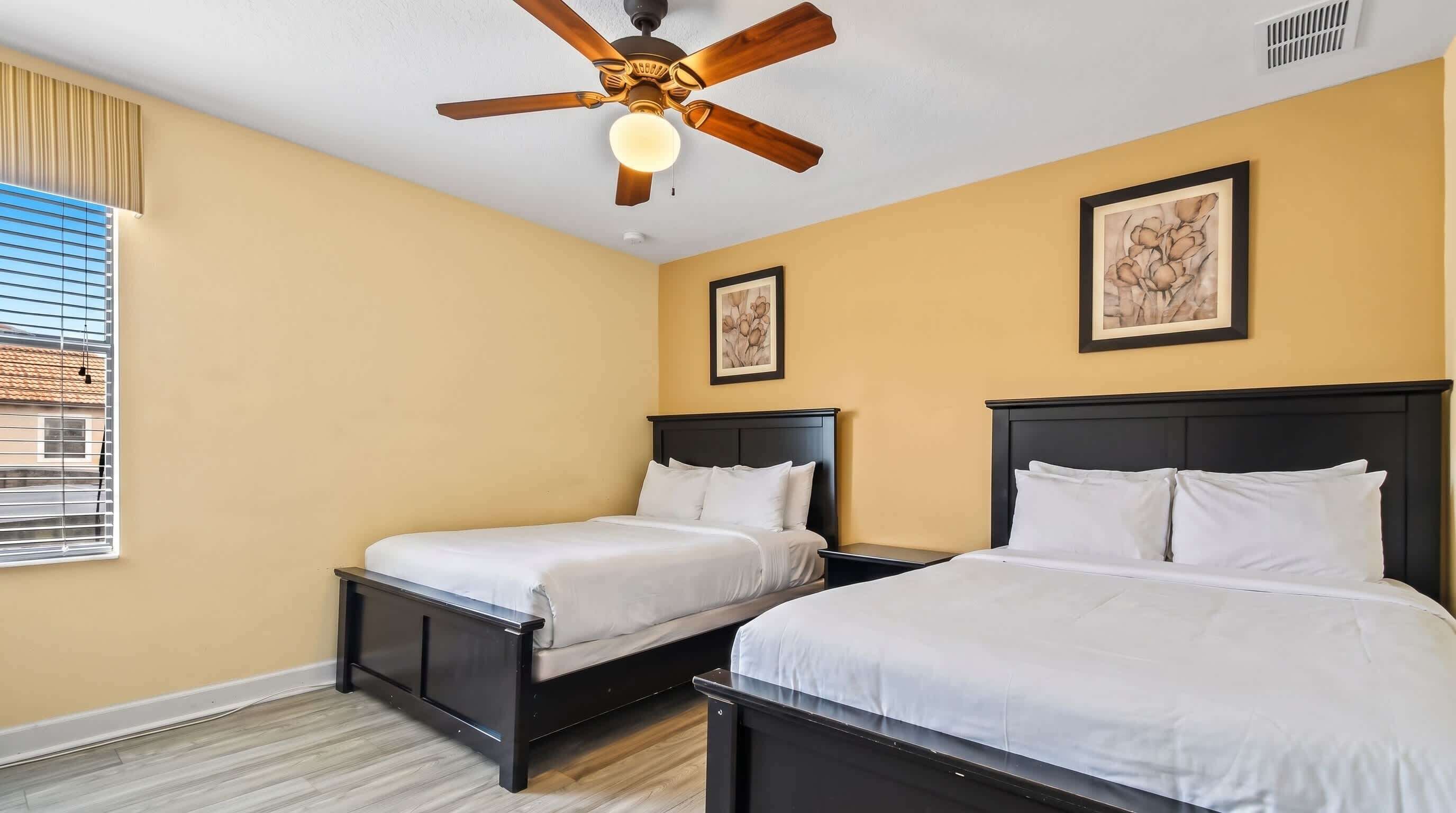A hotel room with two beds, a ceiling fan, and artwork on the walls.