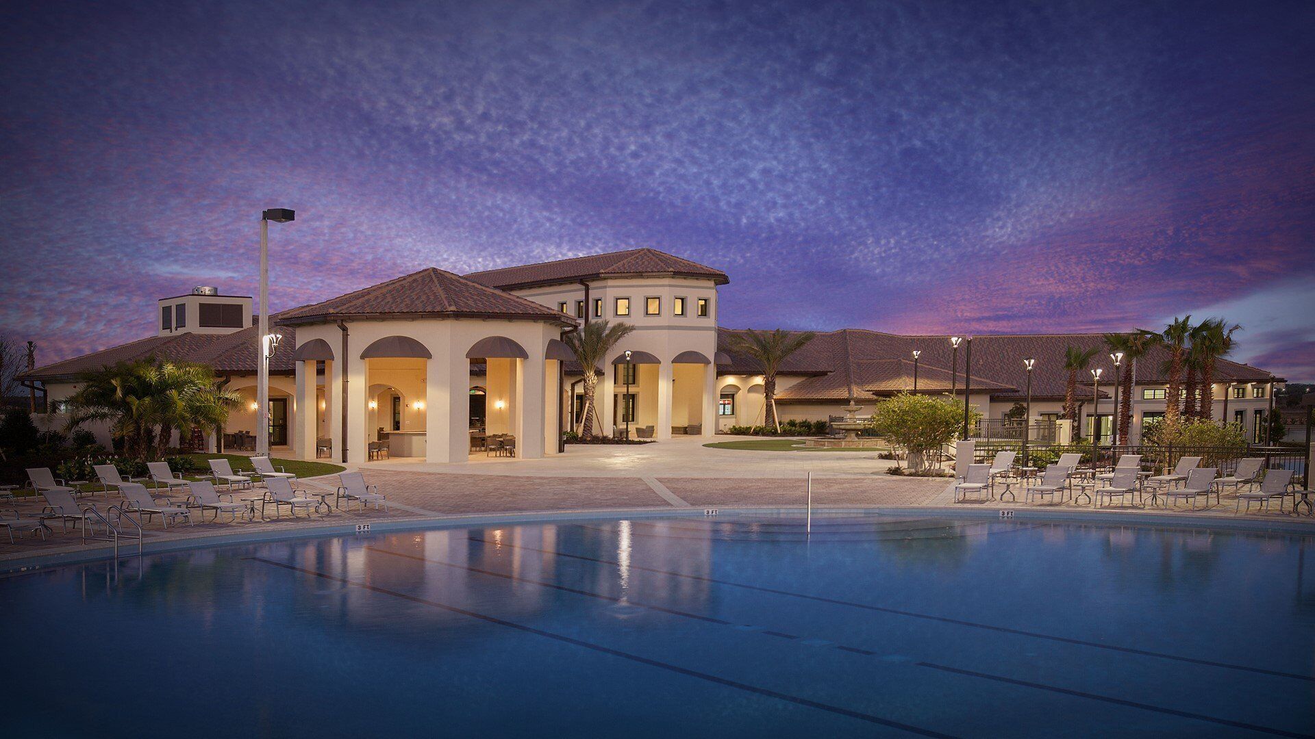 A resort with a swimming pool, lounge chairs, and a building with arched walkways.