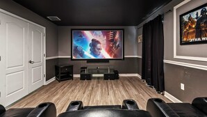 A home theater room with a large flat-screen TV, a wooden floor, and black leather seating.
