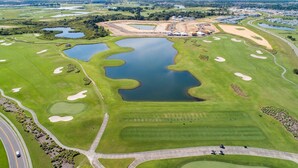 An aerial view of a golf course with multiple ponds, sand bunkers, and a road curving around the course.
