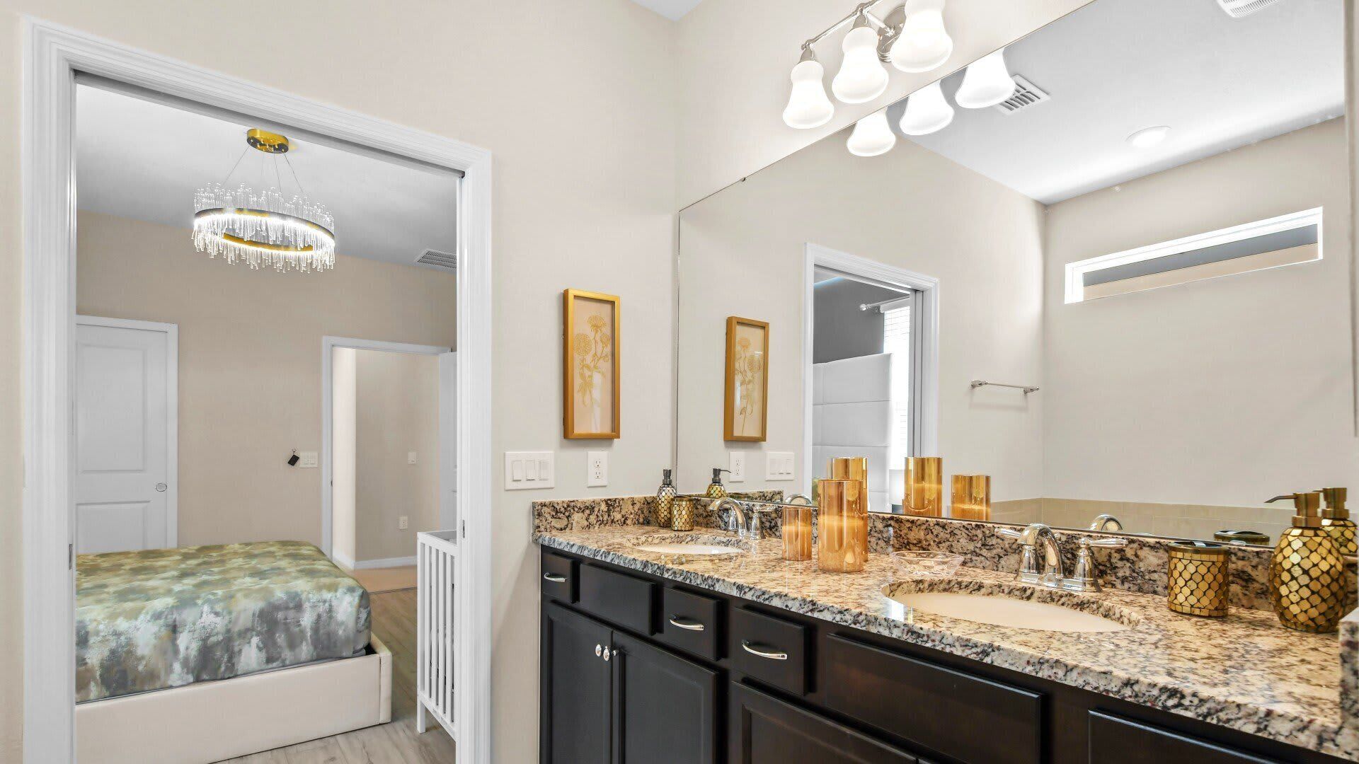 A modern bathroom with a large mirror, granite countertop, and gold fixtures.