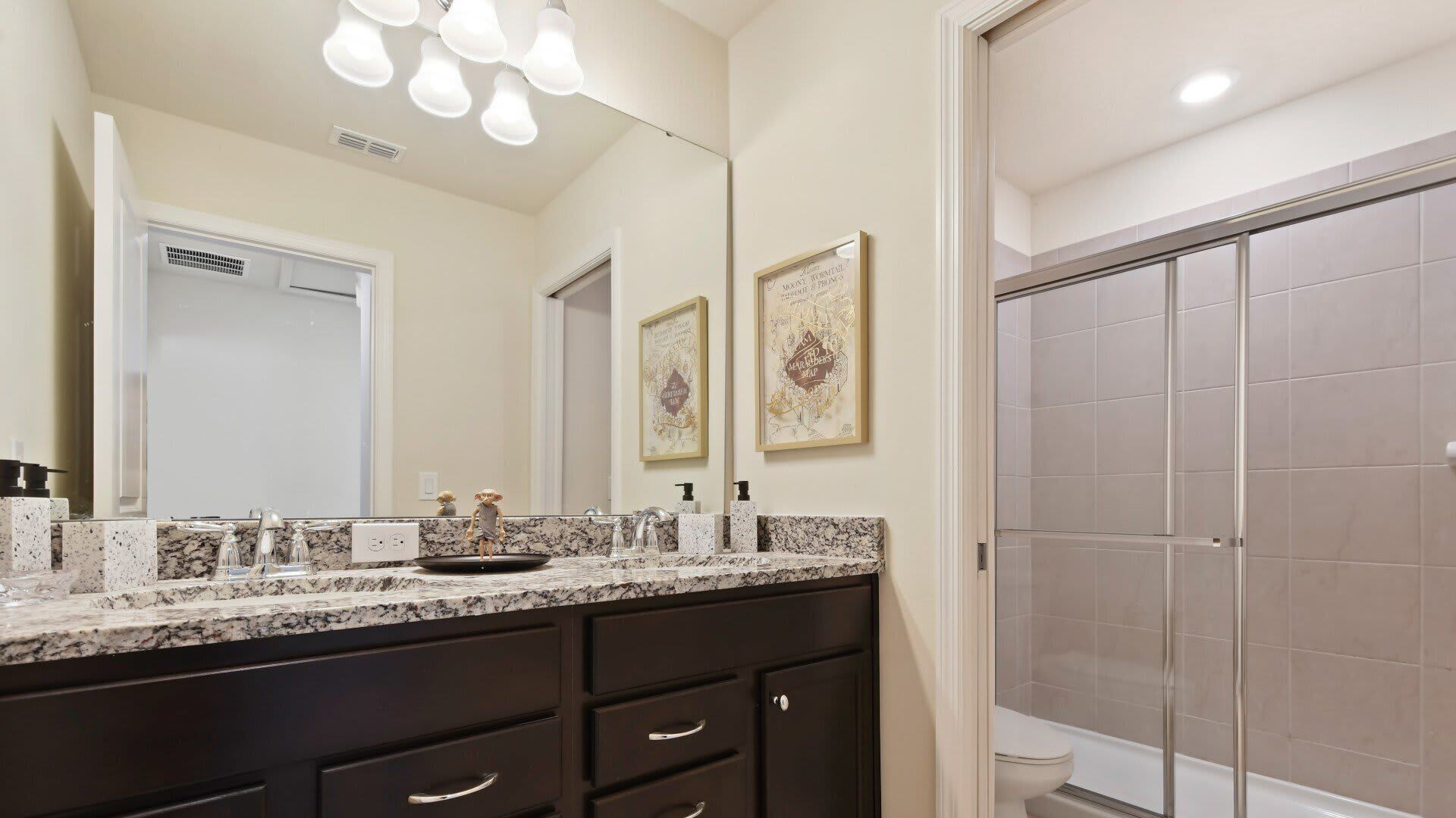A bathroom with a large mirror, a sink with a marble countertop, a dark vanity, and a shower area.
