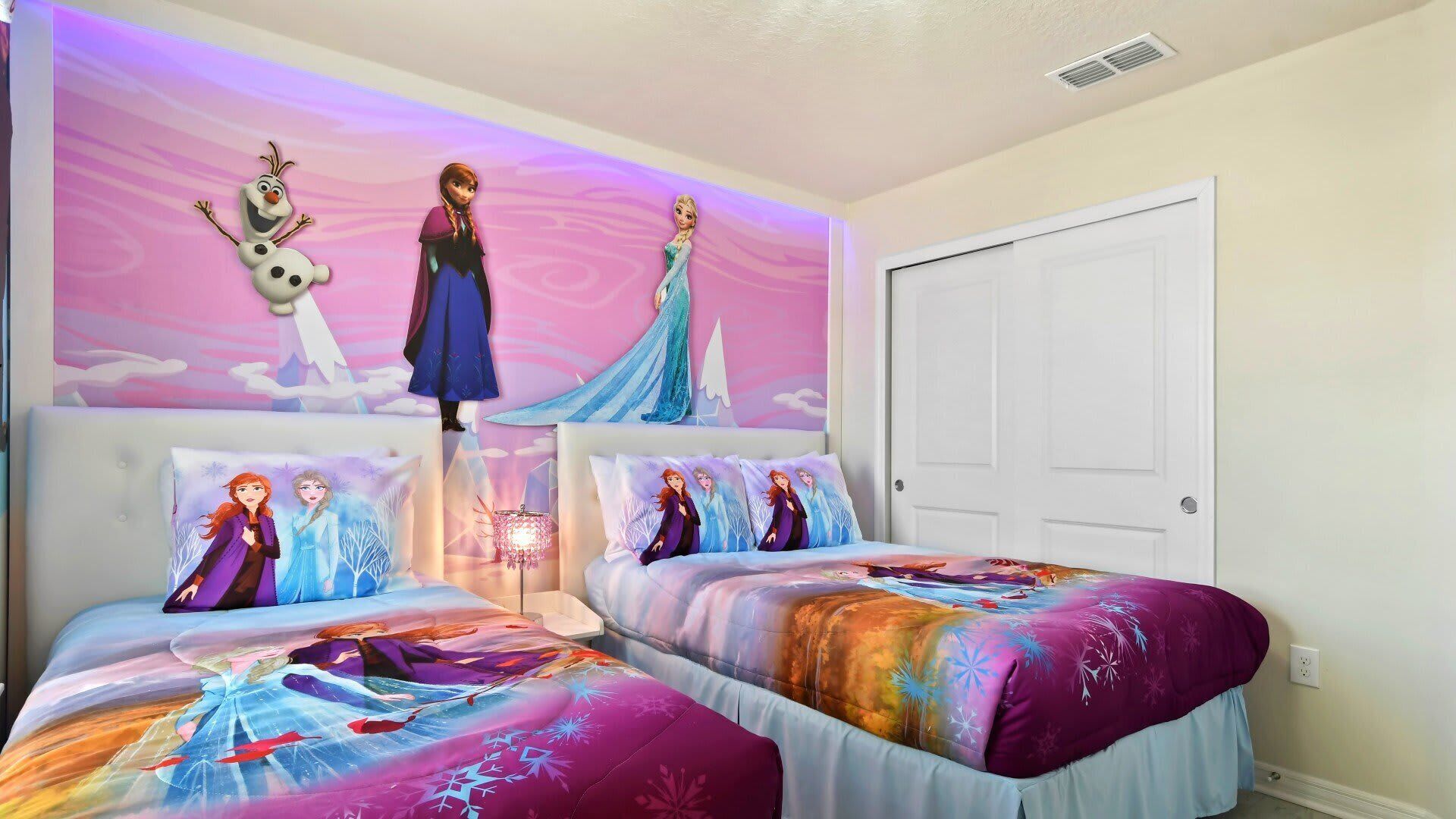 A bedroom with two beds, each with a Frozen-themed duvet cover, a wall mural with Frozen characters, and a chandelier.