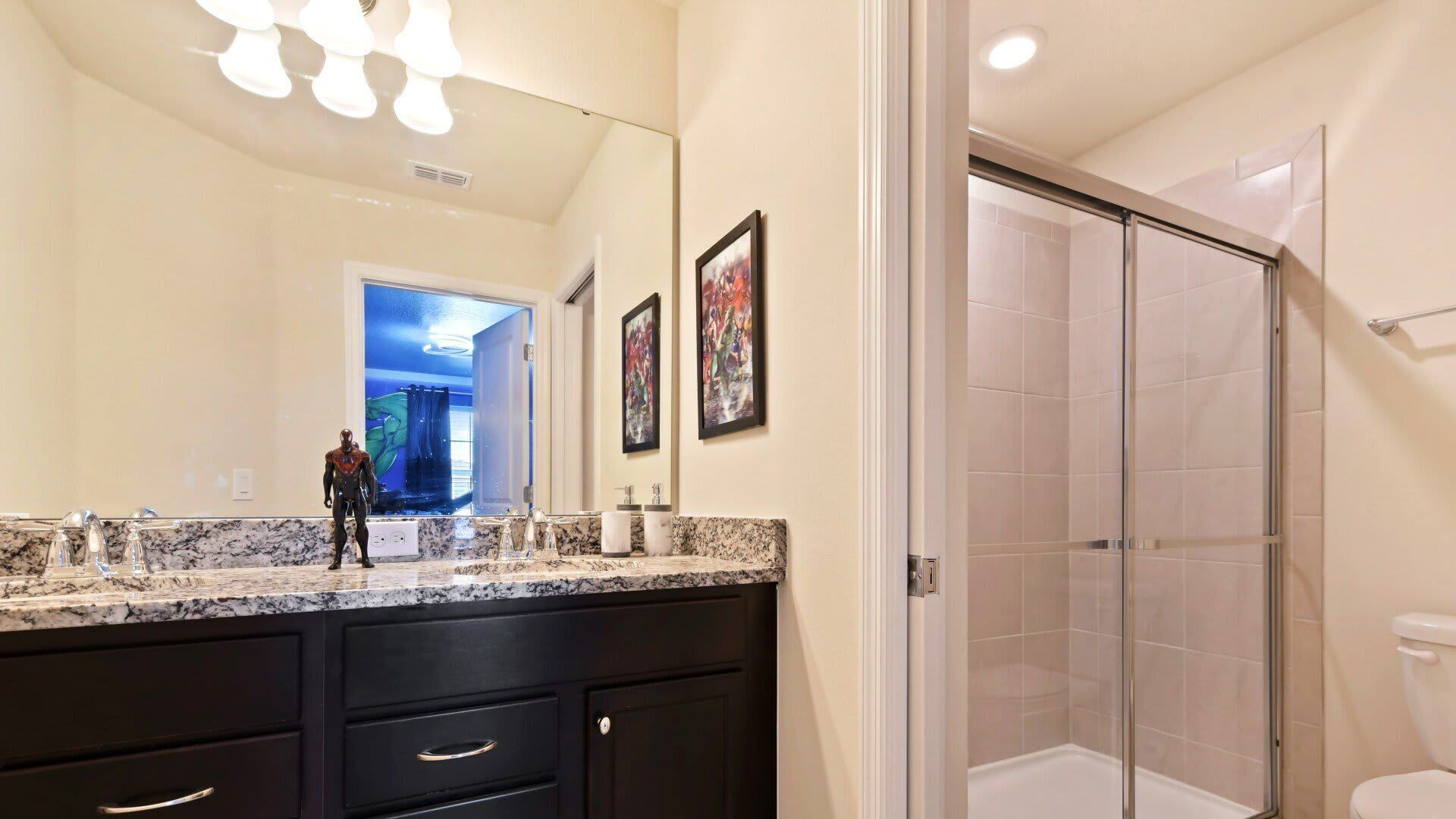 A modern bathroom with a large mirror, marble countertop, and a glass shower enclosure.