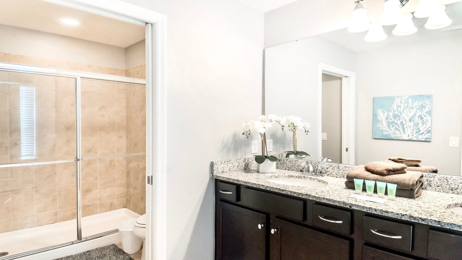 A modern bathroom with a glass shower enclosure, a granite countertop, a sink with a mirror, and a towel rack.