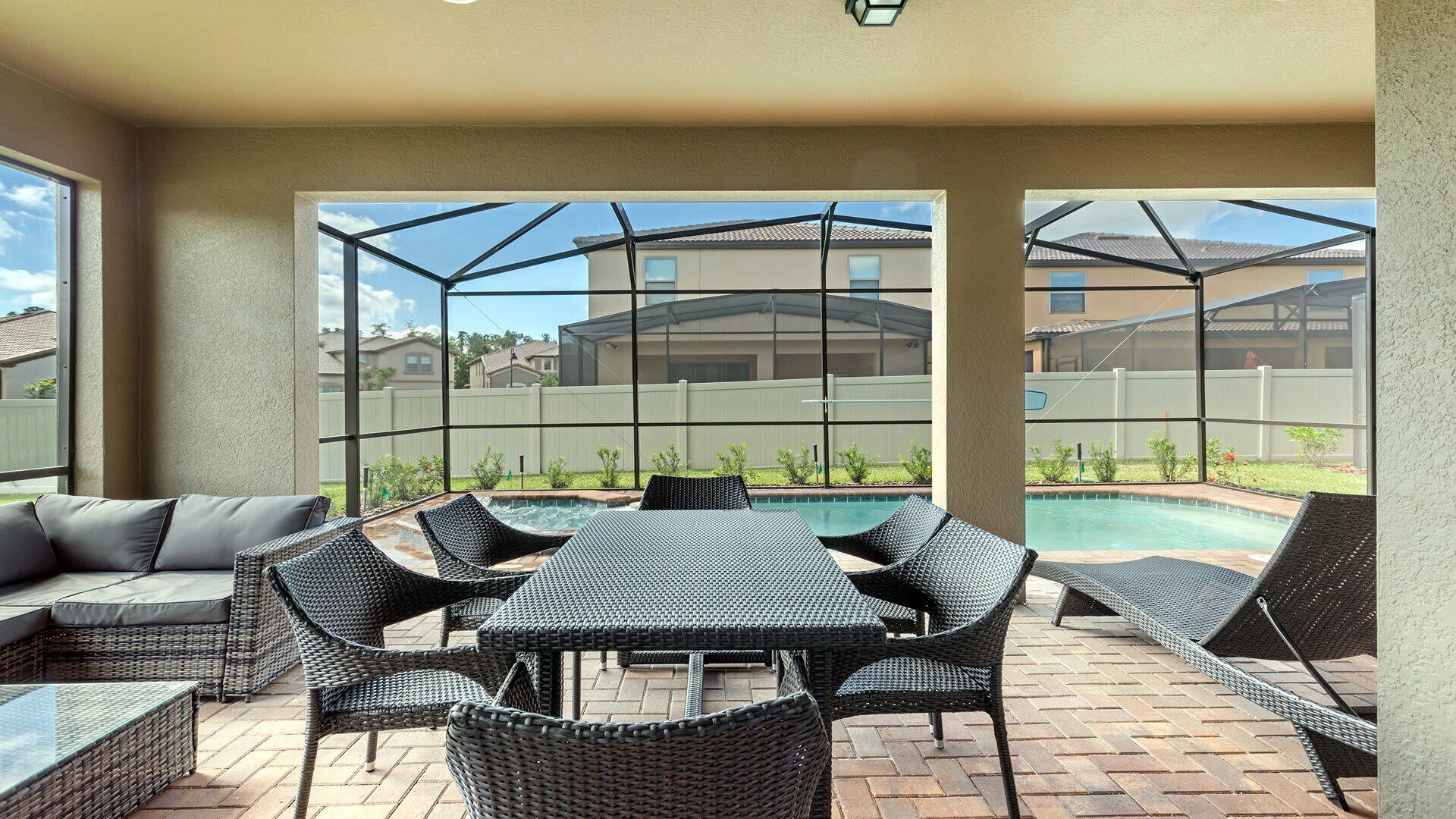 An outdoor patio with a pool, wicker furniture, and a view of neighboring houses.