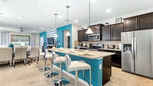 A modern kitchen with a central island, stainless steel appliances, and a blue accent wall. - Special Offer Spacious Home With Pool! (Kissimmee)
