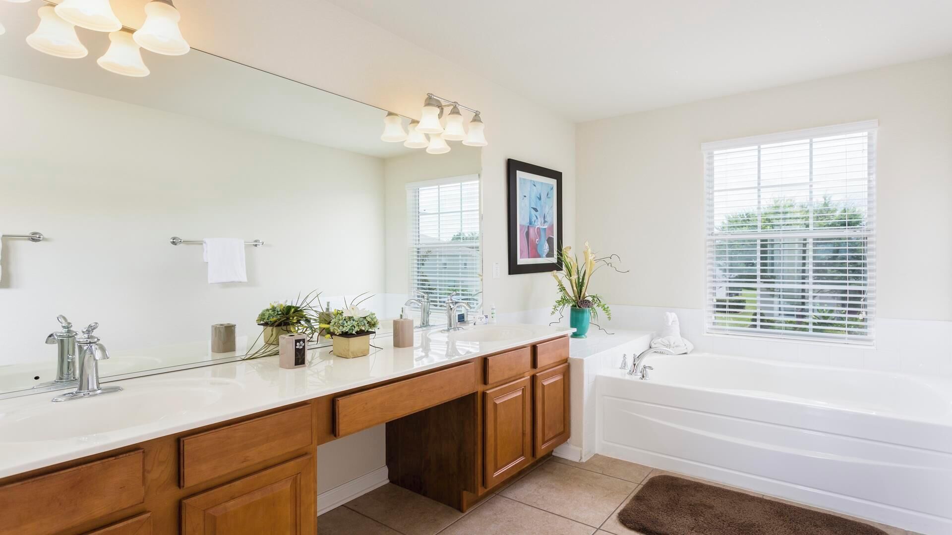 Une salle de bain avec un grand miroir, deux lavabos, une baignoire et une fenêtre avec des stores.