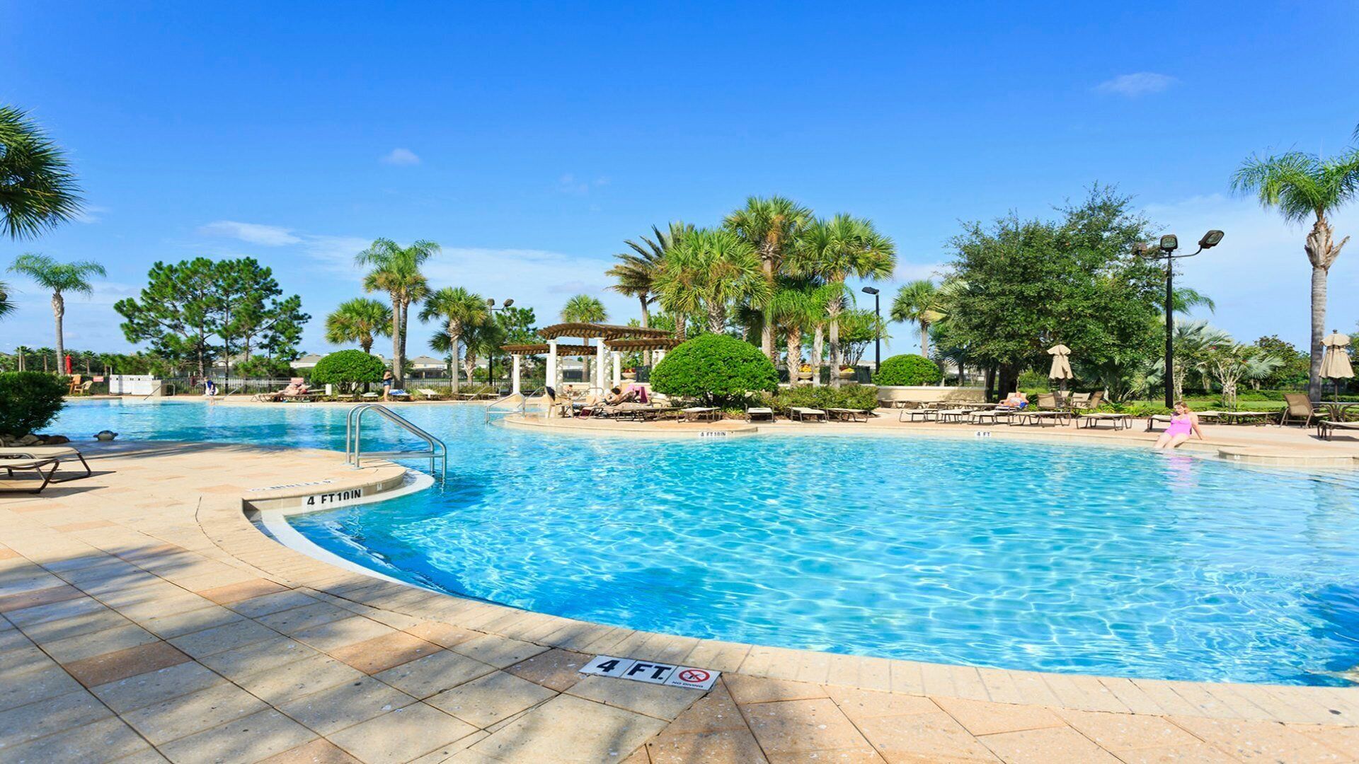 A swimming pool with a 4 ft depth sign, surrounded by palm trees and lounge chairs.