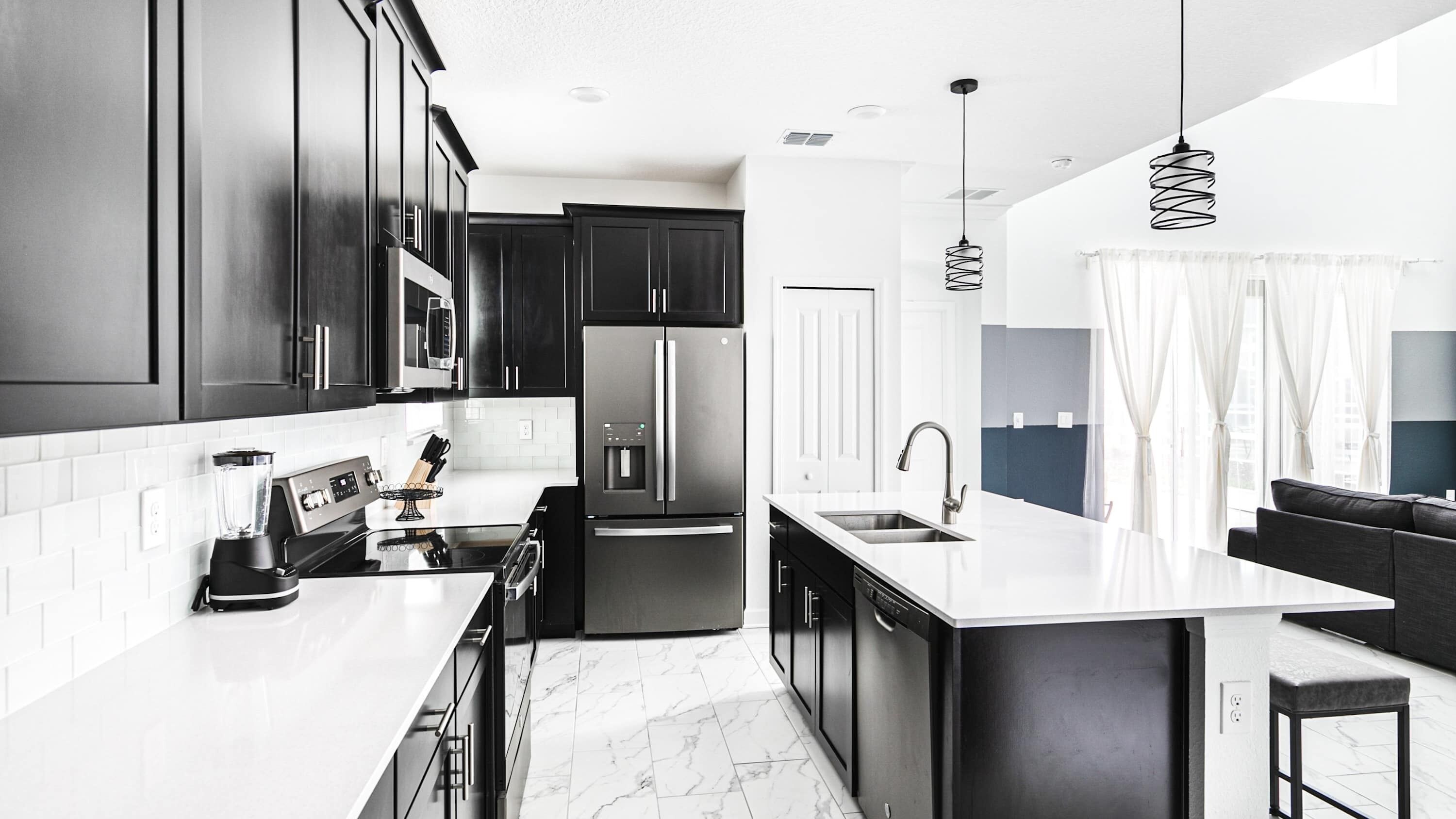A modern kitchen with dark cabinetry, a stainless steel refrigerator, a built-in oven, and a large island with a sink.
