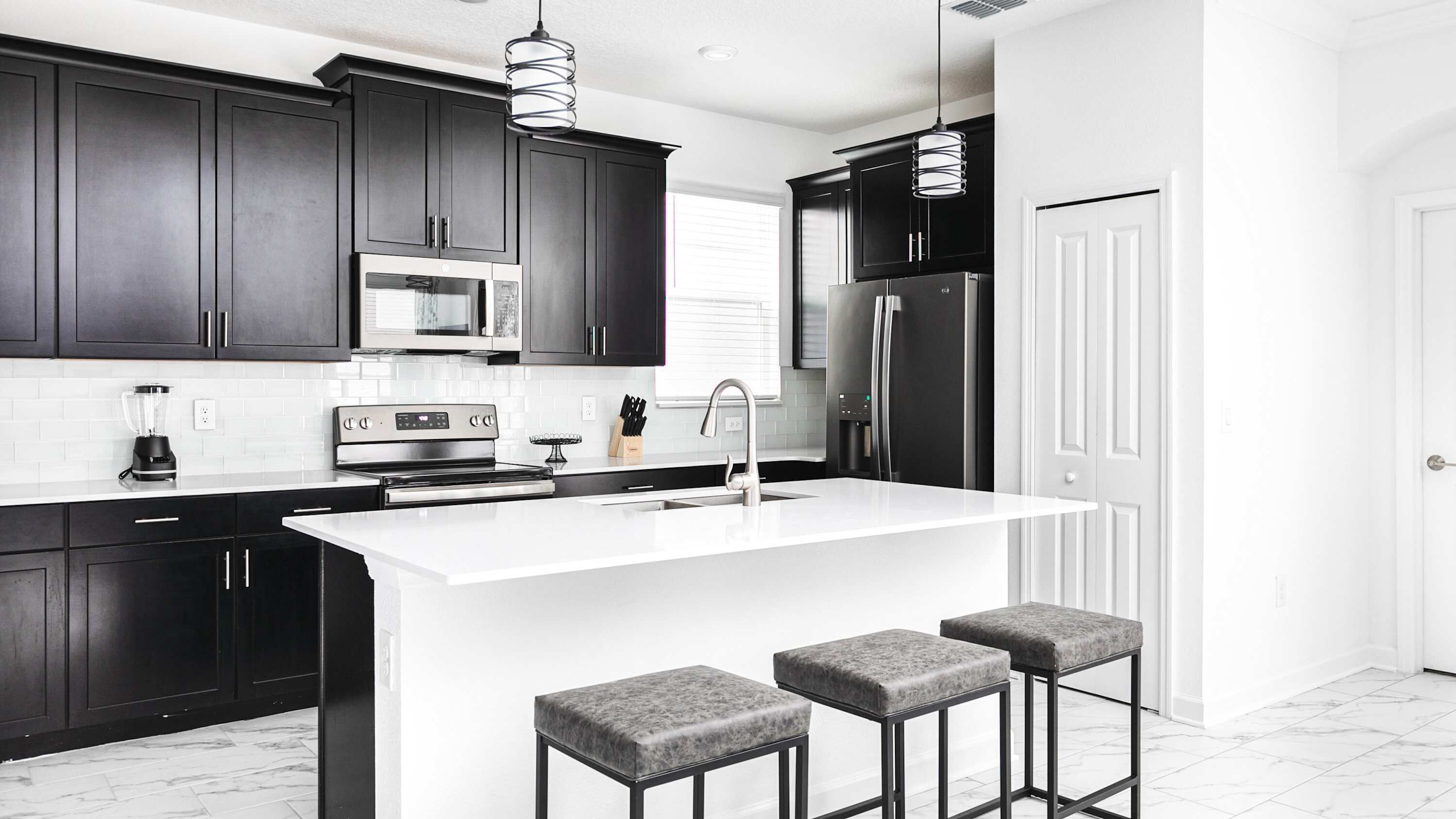 A modern kitchen with dark cabinets, a white island, stainless steel appliances, and bar stools.