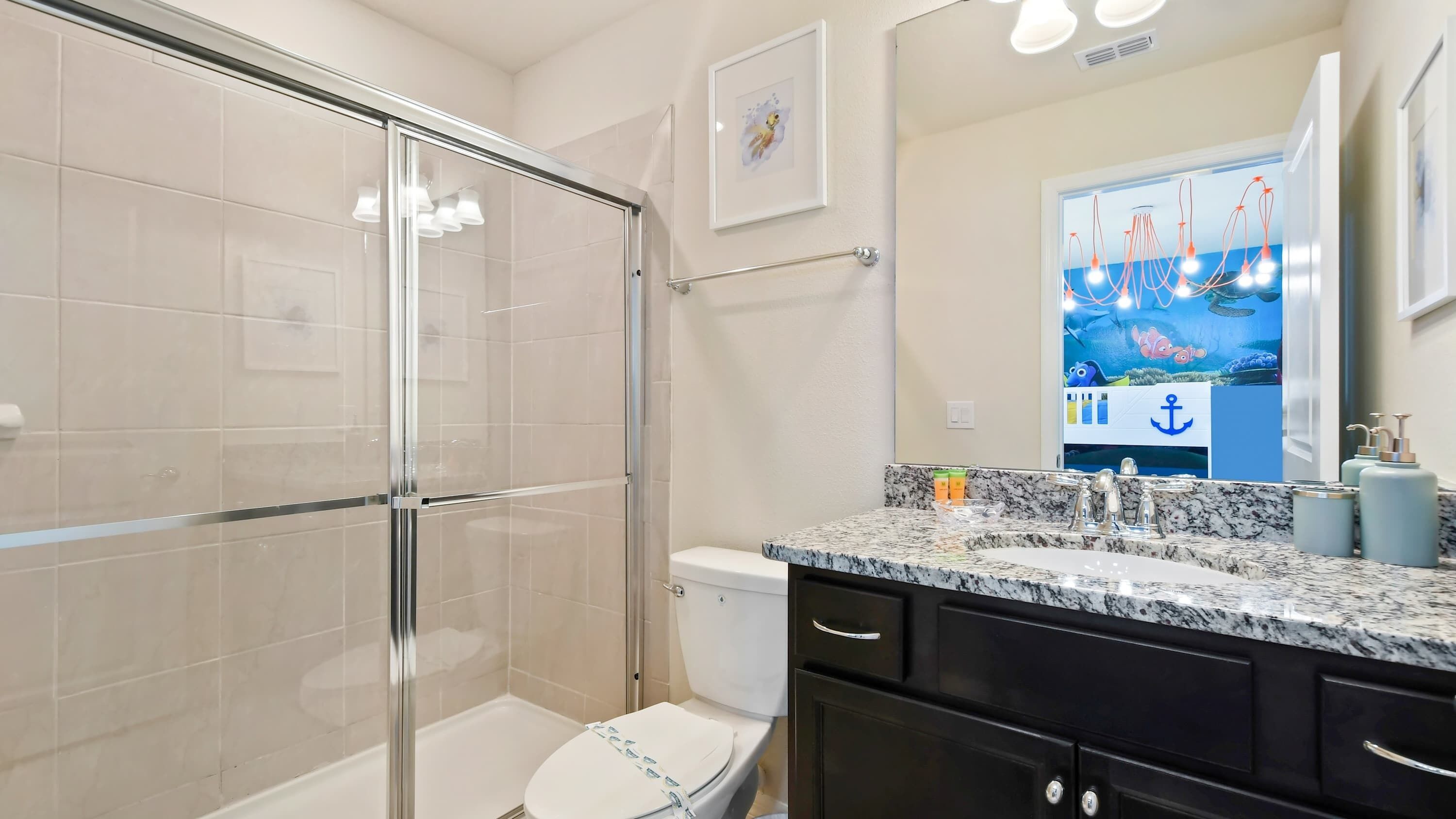 Een moderne badkamer met een glazen douchecabine, toilet en een wastafel met een granieten aanrechtblad.