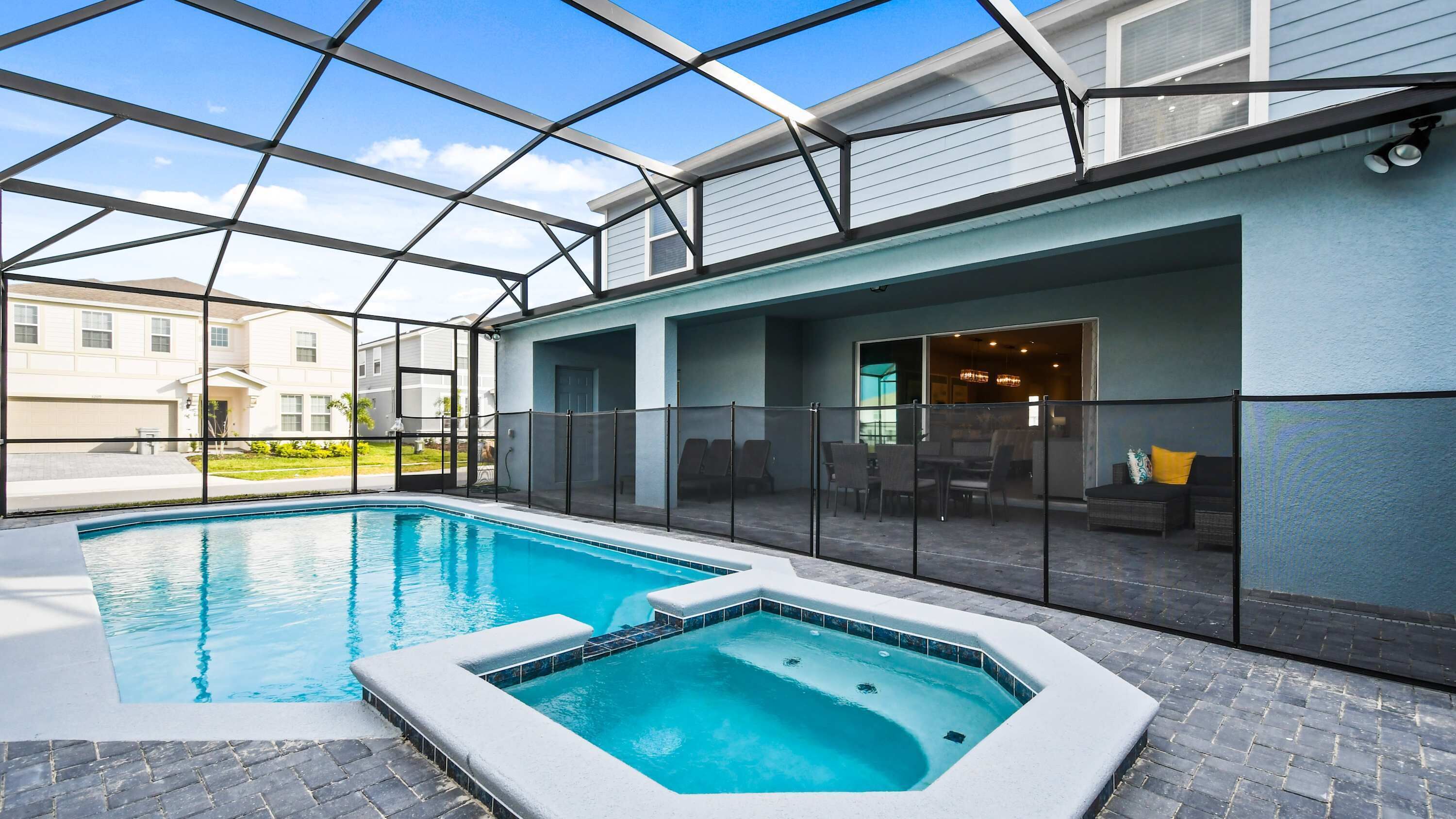 Une piscine avec un jacuzzi, entourée d’une clôture en verre, et un espace patio avec des sièges d’extérieur.