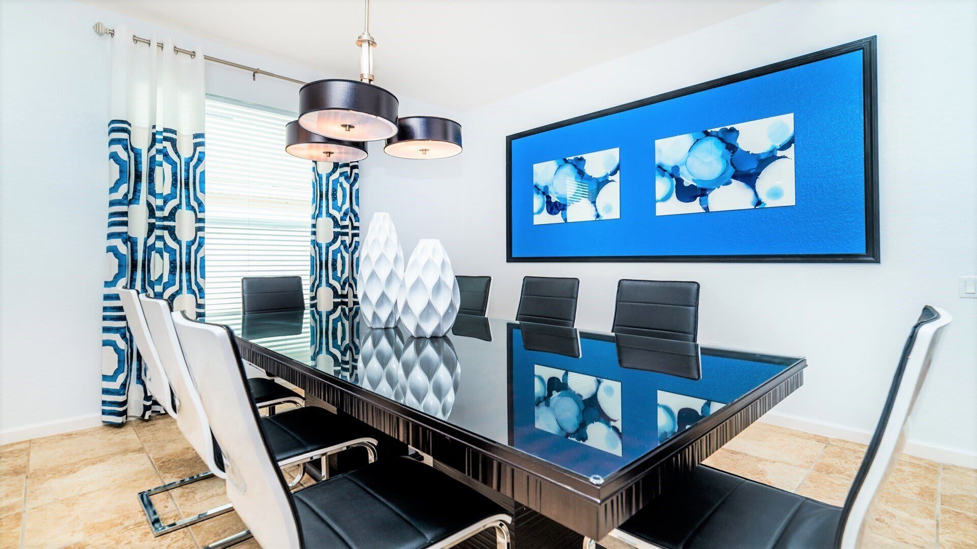 Une salle à manger moderne avec une table en verre, des chaises noires et un tableau abstrait bleu.