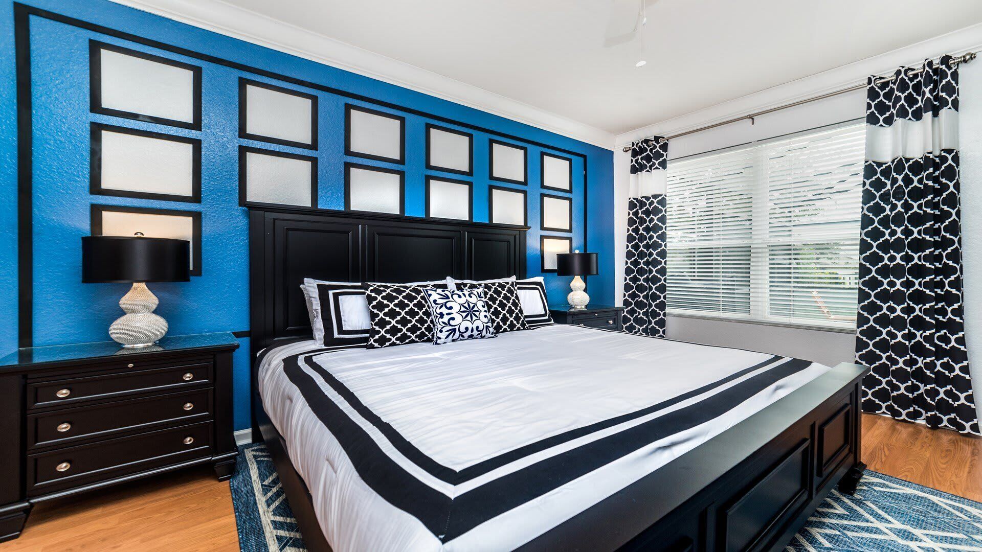 A modern bedroom with a large bed, a blue accent wall, and a patterned window treatment.