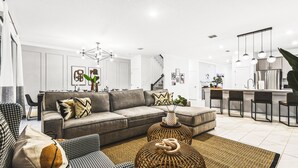 A modern living room with a grey sofa, patterned cushions, and a woven ottoman. - Themed Rooms & Pool in Storey Lake Resort (Kissimmee)