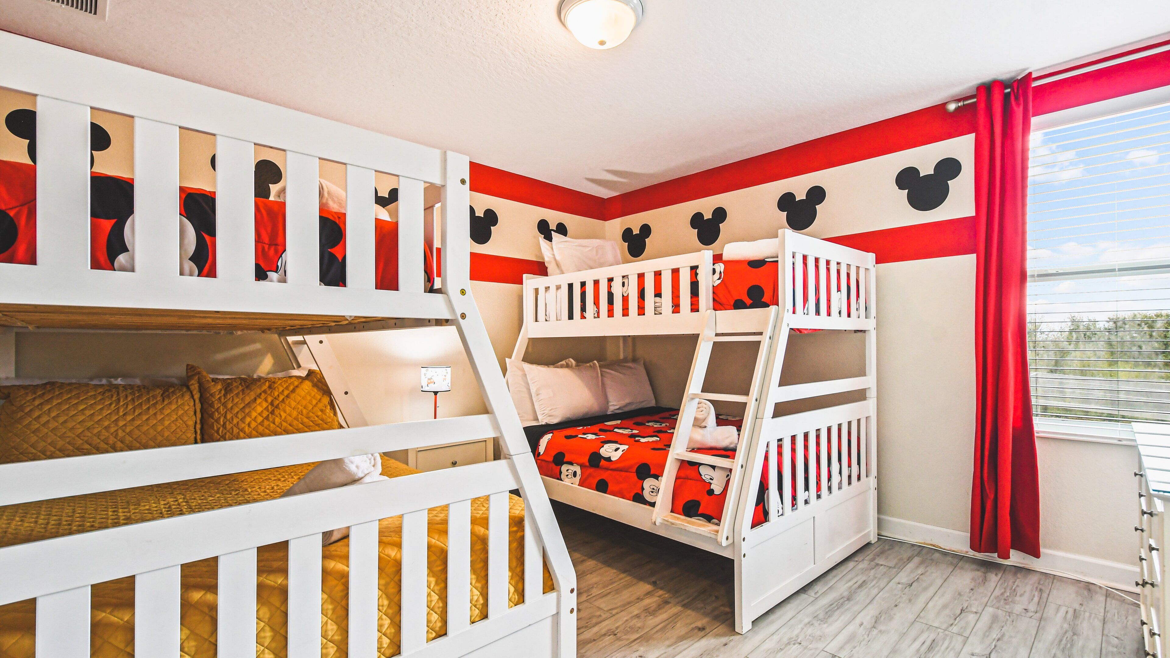 Une chambre avec des lits superposés décorée sur le thème de Mickey Mouse, avec des motifs sur les murs et du linge de lit assorti.