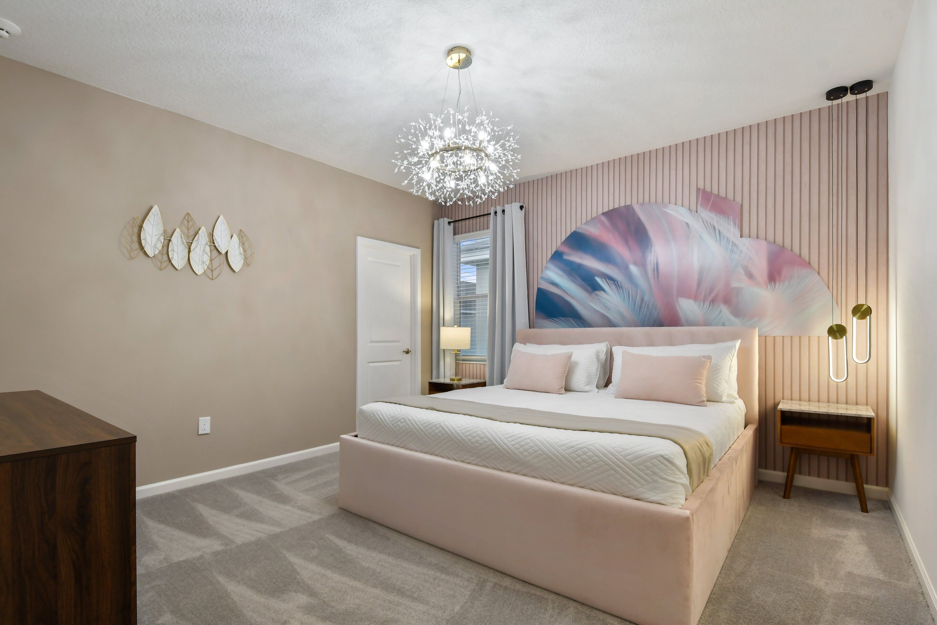 Een slaapkamer met een groot bed, een kroonluchter, een kunstwerk aan de muur en een nachtkastje.
