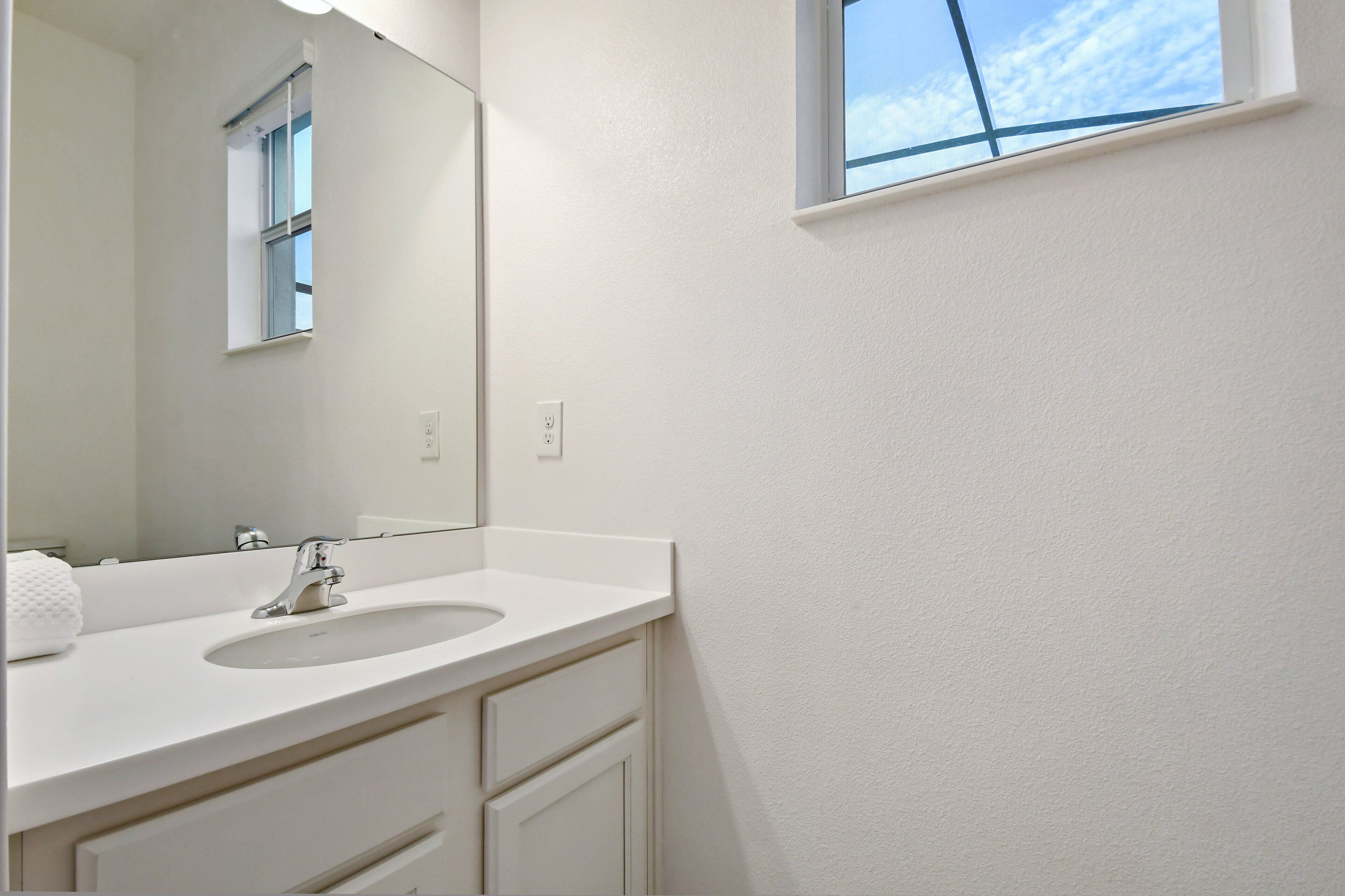 A bathroom with a white sink, a mirror, and a window with a view of the sky.