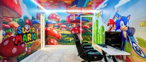 A room with a Mario-themed mural, a gaming chair, a TV, and a Sonic the Hedgehog figure.