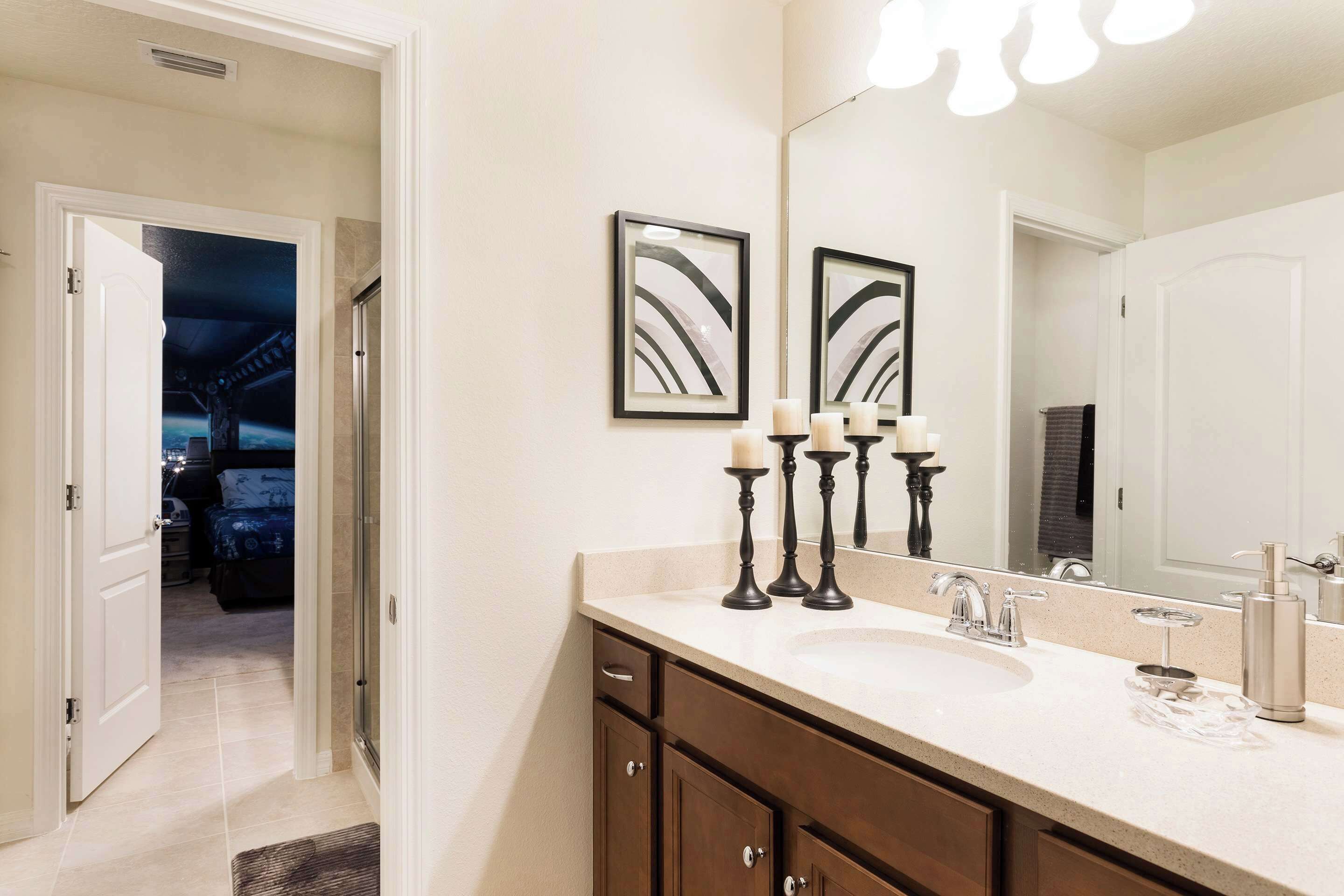 A bathroom with a large mirror, a sink, and a door leading to a bedroom.