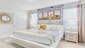 Une chambre moderne avec un grand lit, une table de chevet avec une lampe, un miroir et une œuvre d’art accrochée au mur.