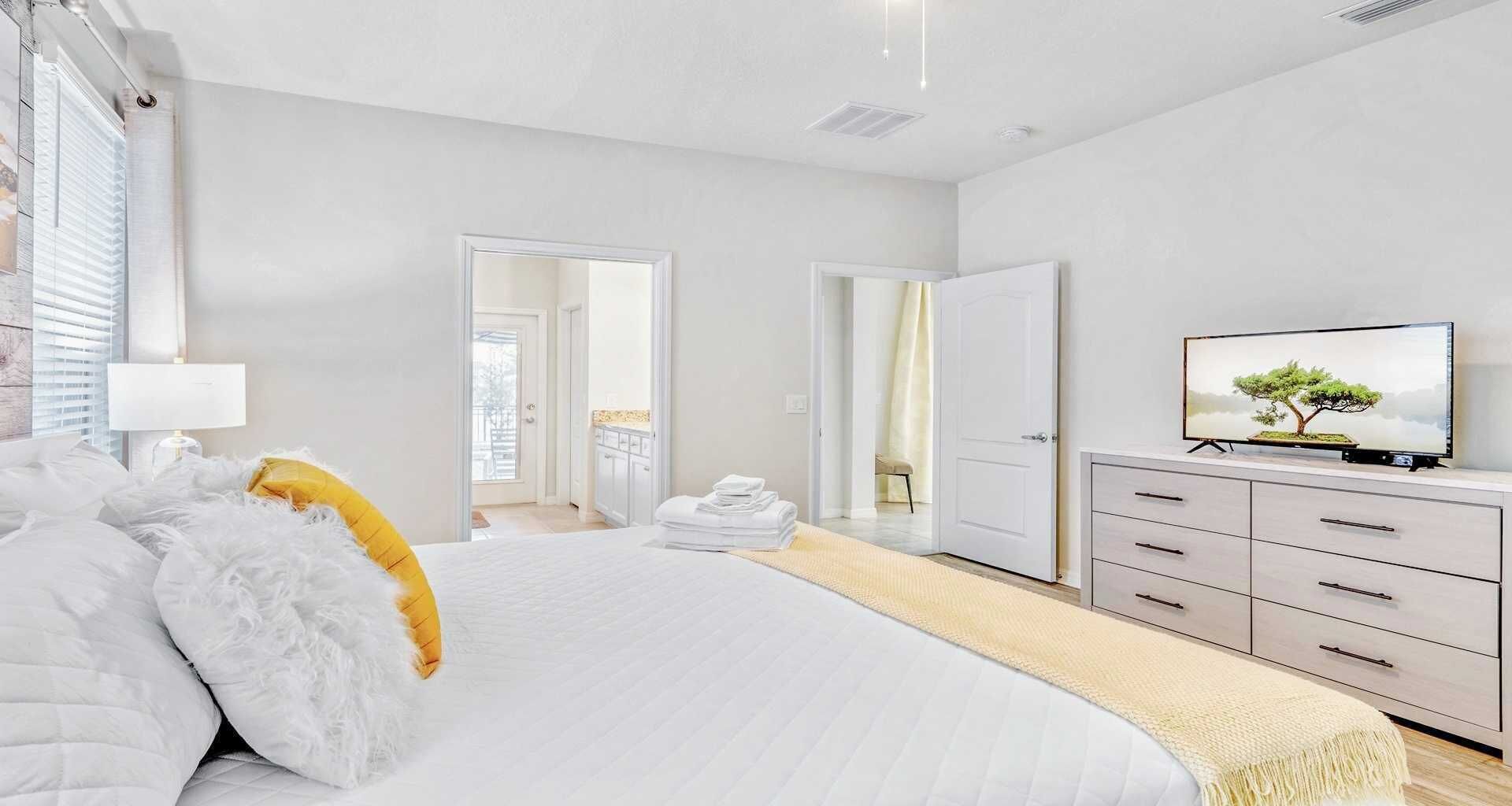 A modern bedroom with a large bed, a TV on a dresser, and a view of the outside through a door.