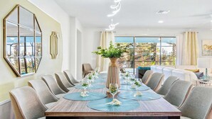 Un espace repas avec une longue table dressée pour un repas, entourée de chaises, et une grande fenêtre offrant une vue sur l’extérieur.