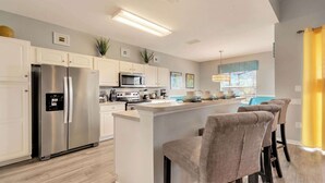 A modern kitchen with white cabinetry, stainless steel appliances, and a central island with bar stools.