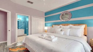 A bedroom with a bed, a bedside table with a lamp, a mirror on the wall, and a bathroom with a sink and mirror.