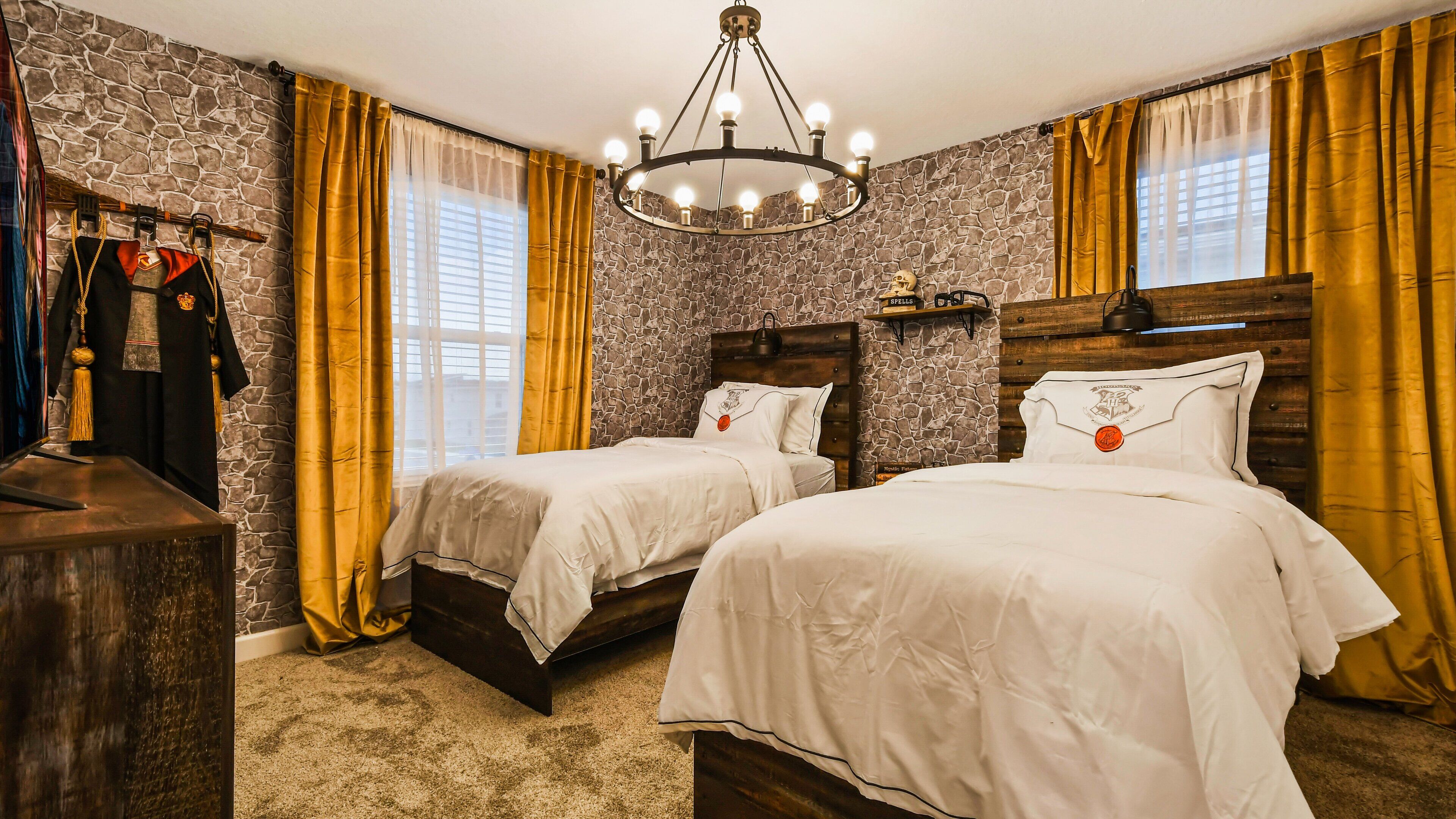A hotel room with two beds, a chandelier, stone wall, and a wardrobe with robes.