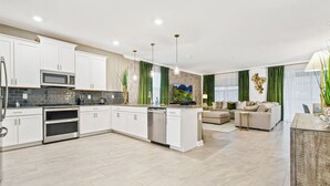 A modern kitchen with white cabinets, a microwave, and a dishwasher. There is a dining area with a sofa and a table.