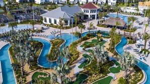 A resort with multiple swimming pools, a golf course, and a large building with a red roof.