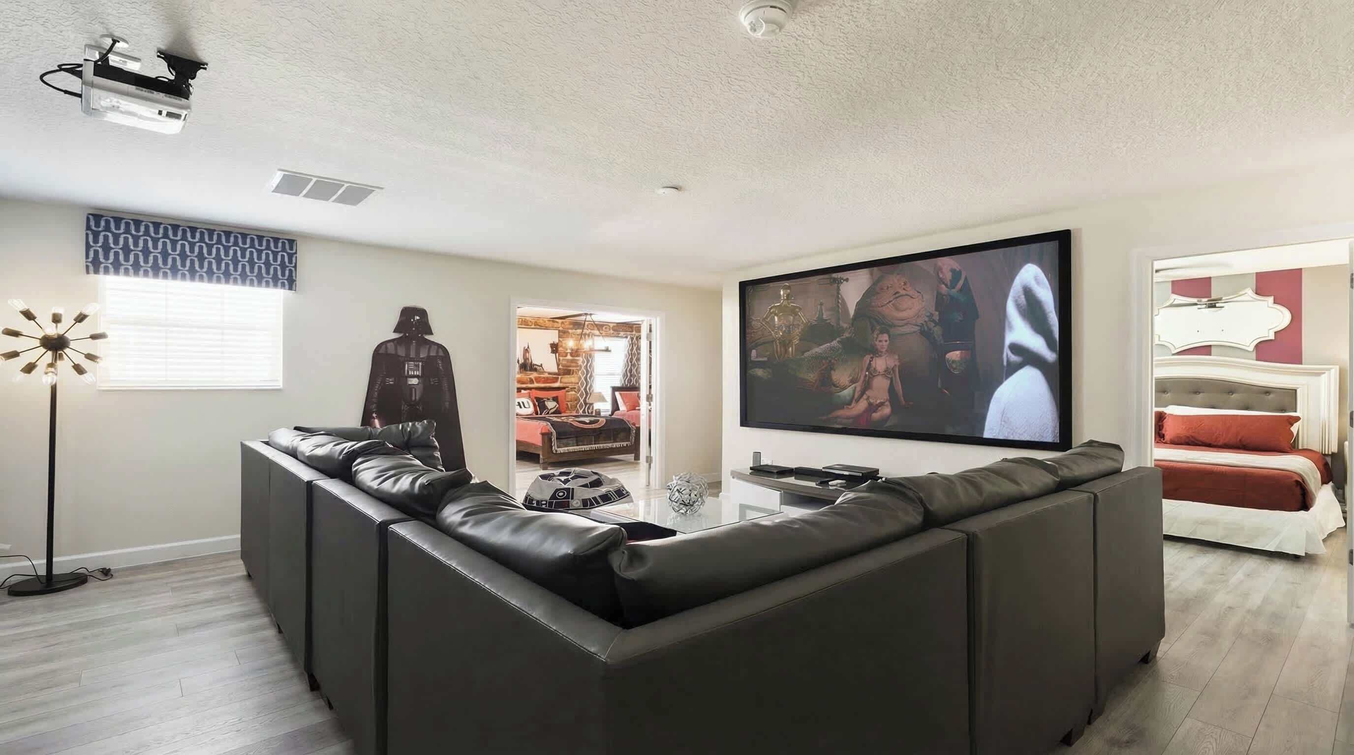 A modern living room with a sectional sofa, a flat-screen TV, a Darth Vader poster, and a Star Wars-themed lamp.