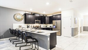 Une cuisine moderne avec des meubles de couleur sombre, un grand îlot central et des appareils électroménagers en acier inoxydable.