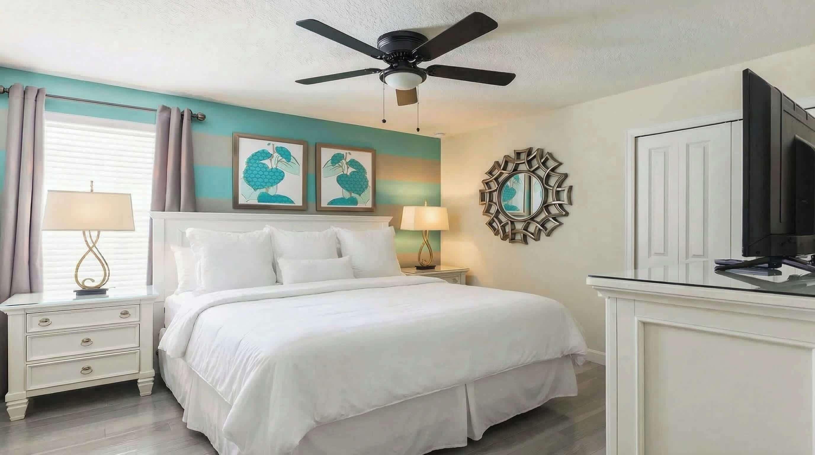 A bedroom with a bed, a ceiling fan, a TV, and artwork on the walls.