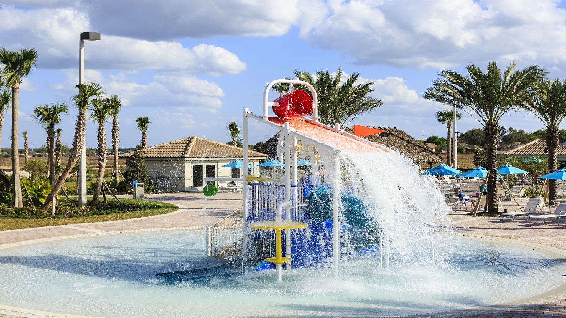 Ein Wasserspielbereich mit einer roten Rutsche, umgeben von Palmen und einem Pool.