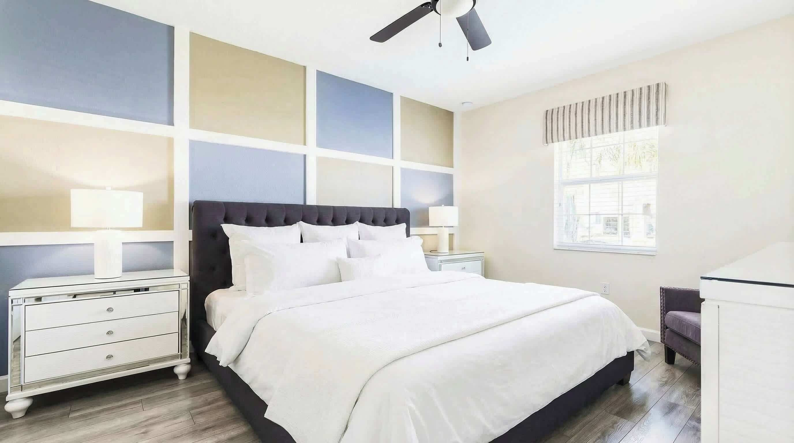 A bedroom with a bed, nightstands, a desk, a ceiling fan, and a window.