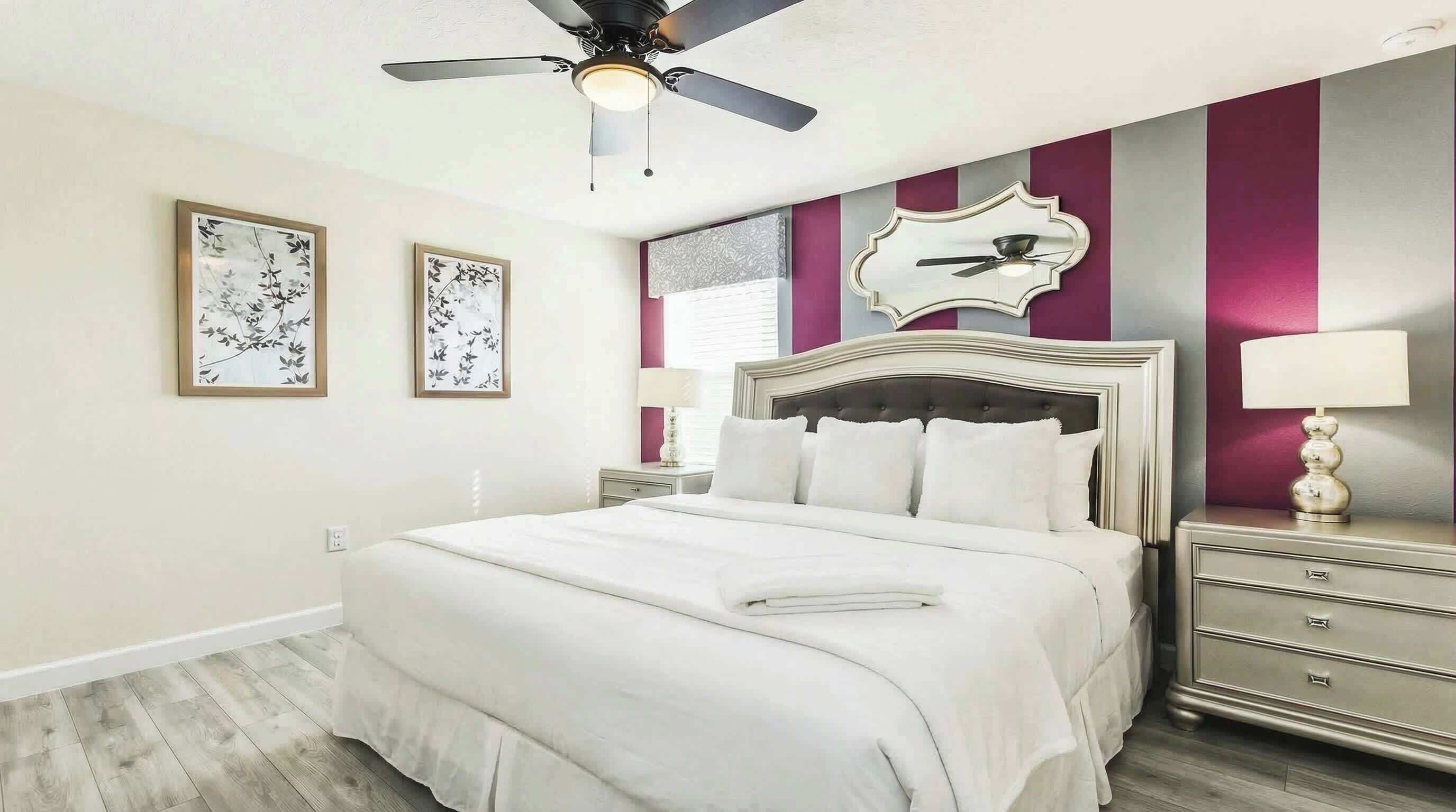 Une chambre à coucher comprenant un lit, une commode, un ventilateur de plafond et deux lampes fixées au mur.