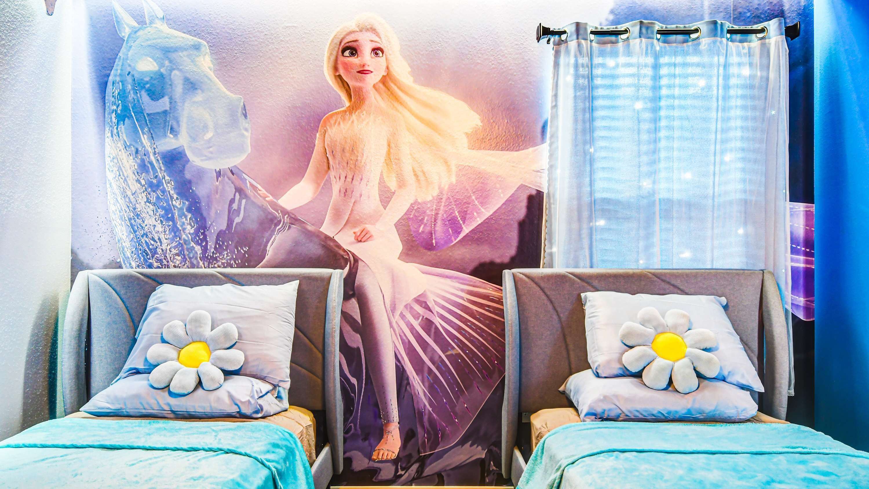 A hotel room with two beds, each with a flower pillow and a blue blanket.