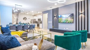 A modern living room with a dining area, a kitchen, and a large flat-screen TV on the wall. - Spacious Home Near Disney With Resort Amenities (Davenport)