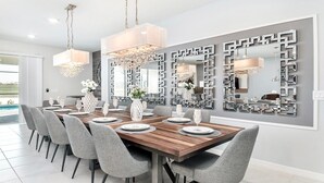 A dining area with a wooden table set for six, grey upholstered chairs, and a large wall mirror with geometric patterns. - Windsor Island Let's Make Sunny Memories 2316 (Davenport)