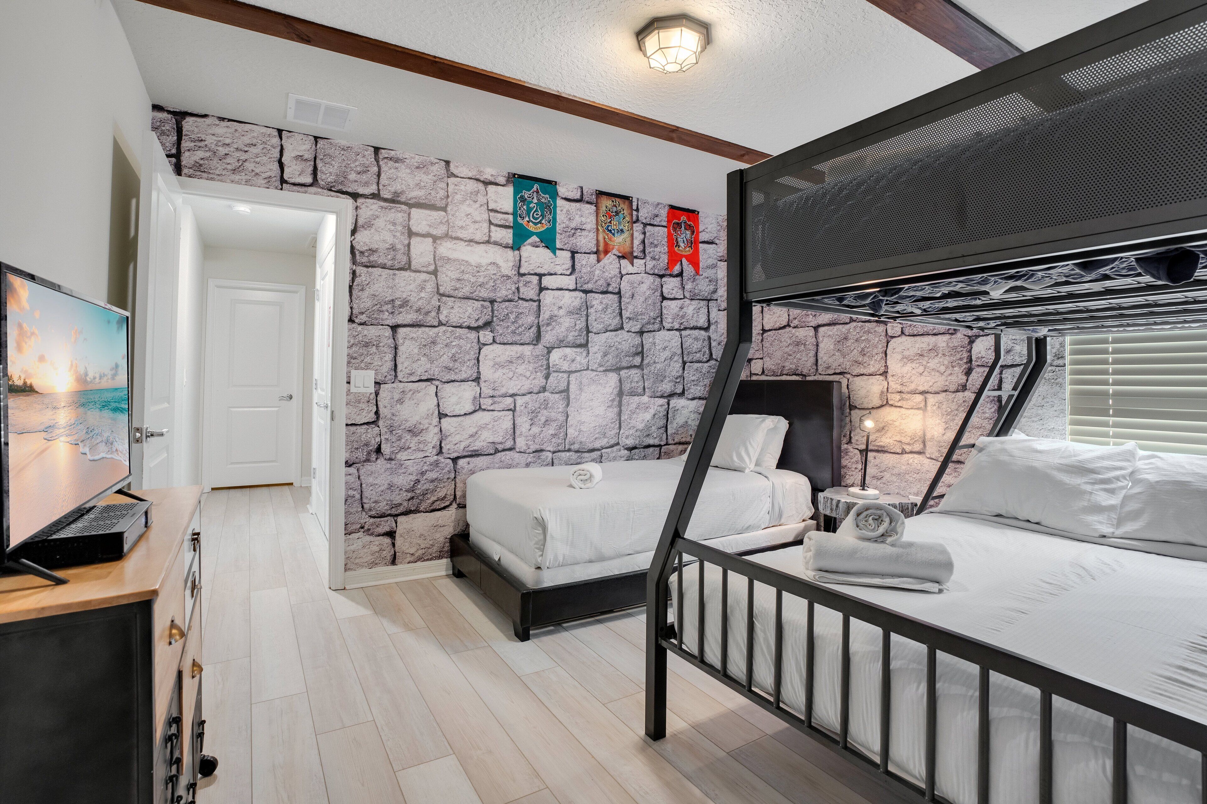 A bedroom with a stone wall, bunk beds, a television, and a door leading to another room.